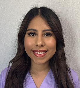 A woman in a purple scrub top is smiling for the camera.