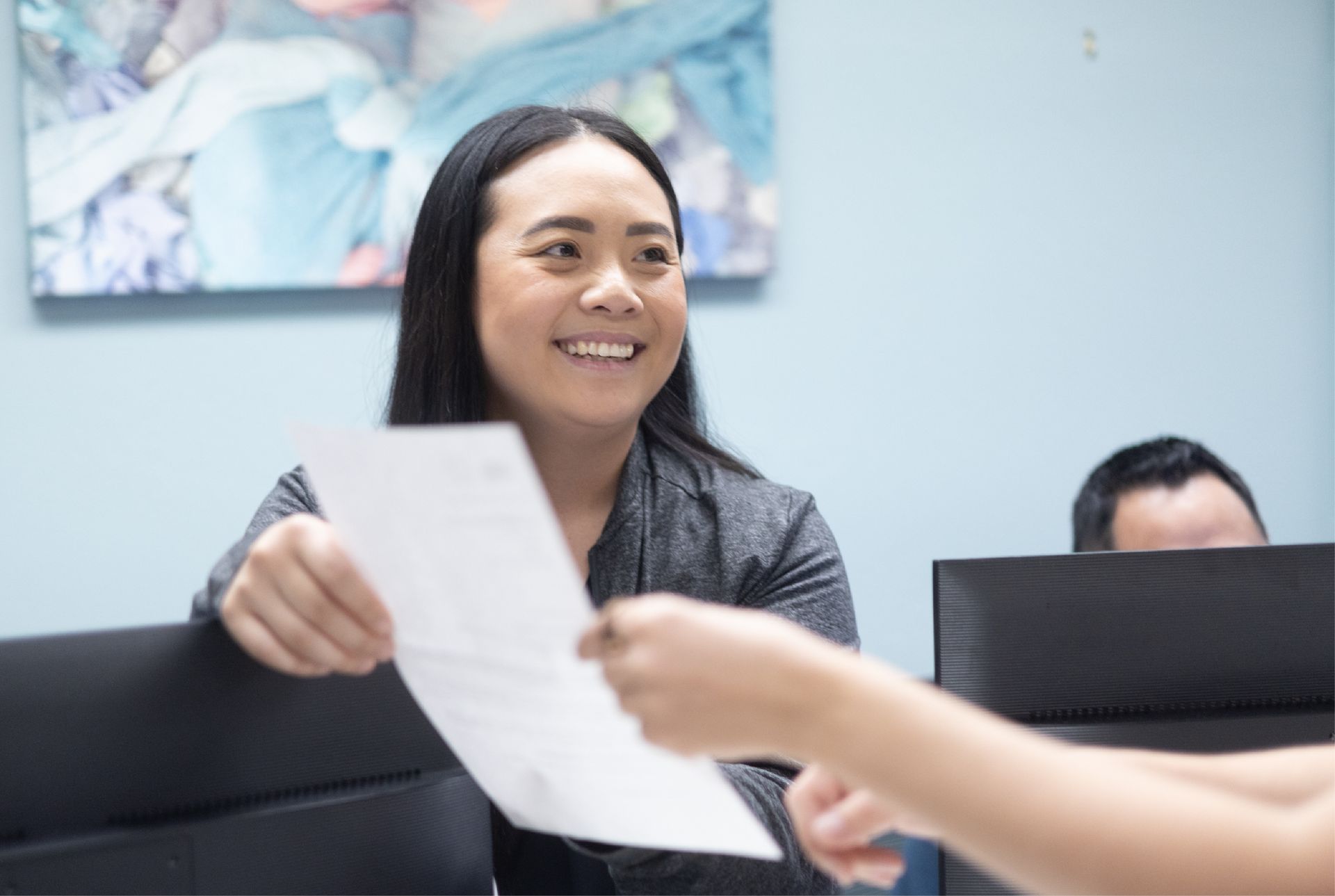 A person is holding a healthcare form in front of a laptop computer.