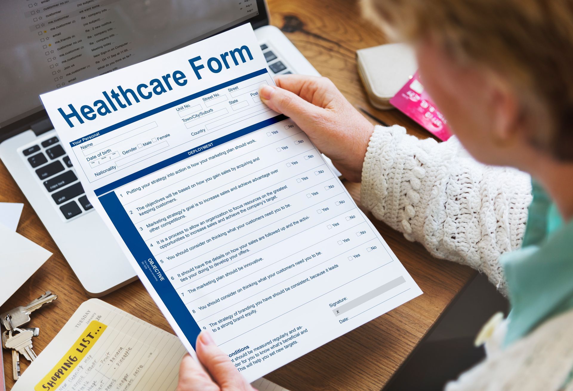 A person is holding a healthcare form in front of a laptop computer.