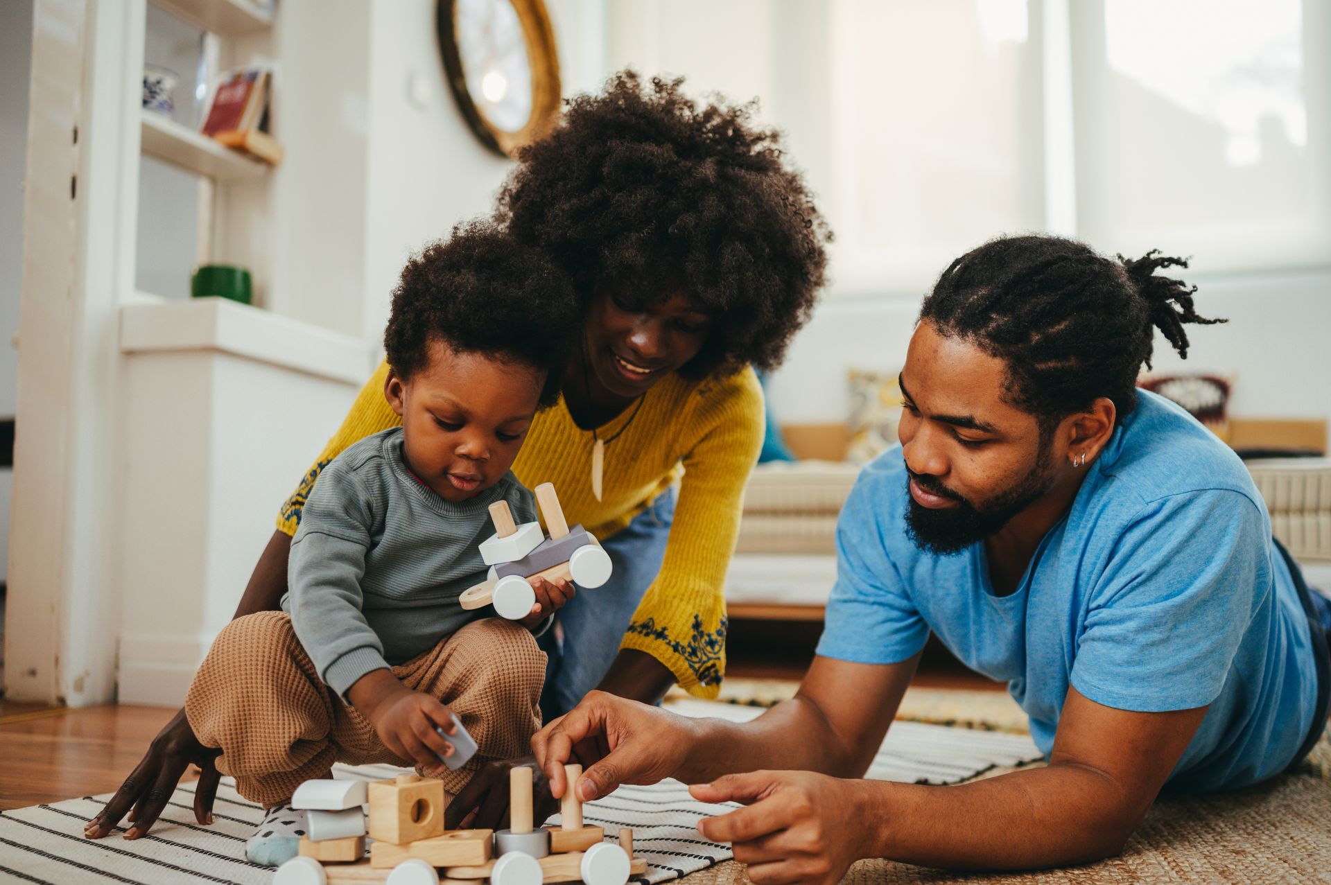 A man , woman and child are playing with wooden blocks on the floor.