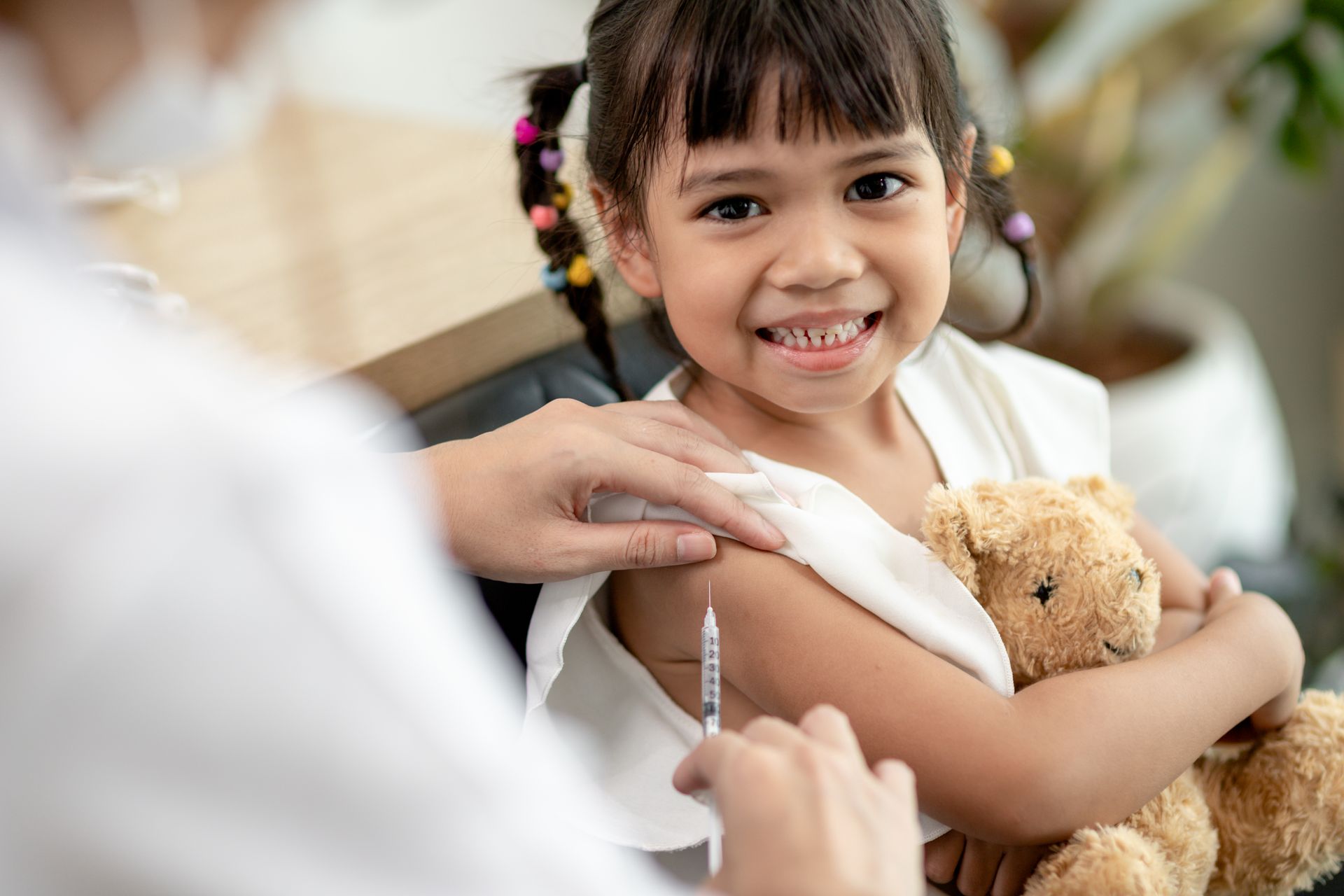 A little girl is getting an injection in her arm while holding a teddy bear.