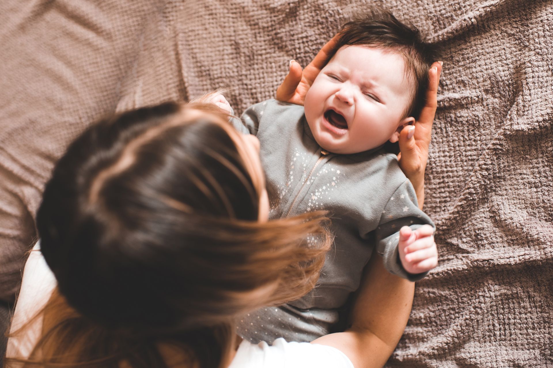 A woman is holding a crying baby on a bed.