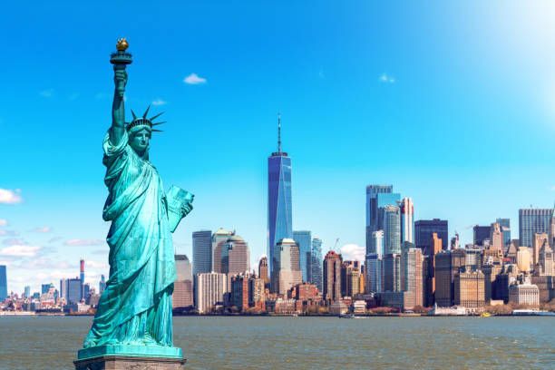 The statue of liberty is in front of the new york city skyline.
