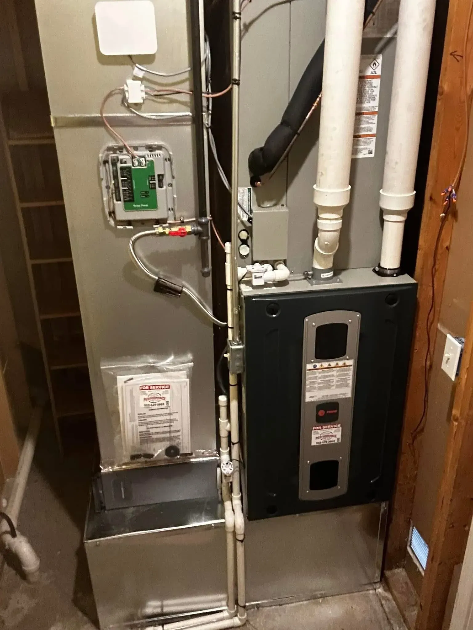 Utility room with furnace, pipes, and electrical panel in a narrow closet.