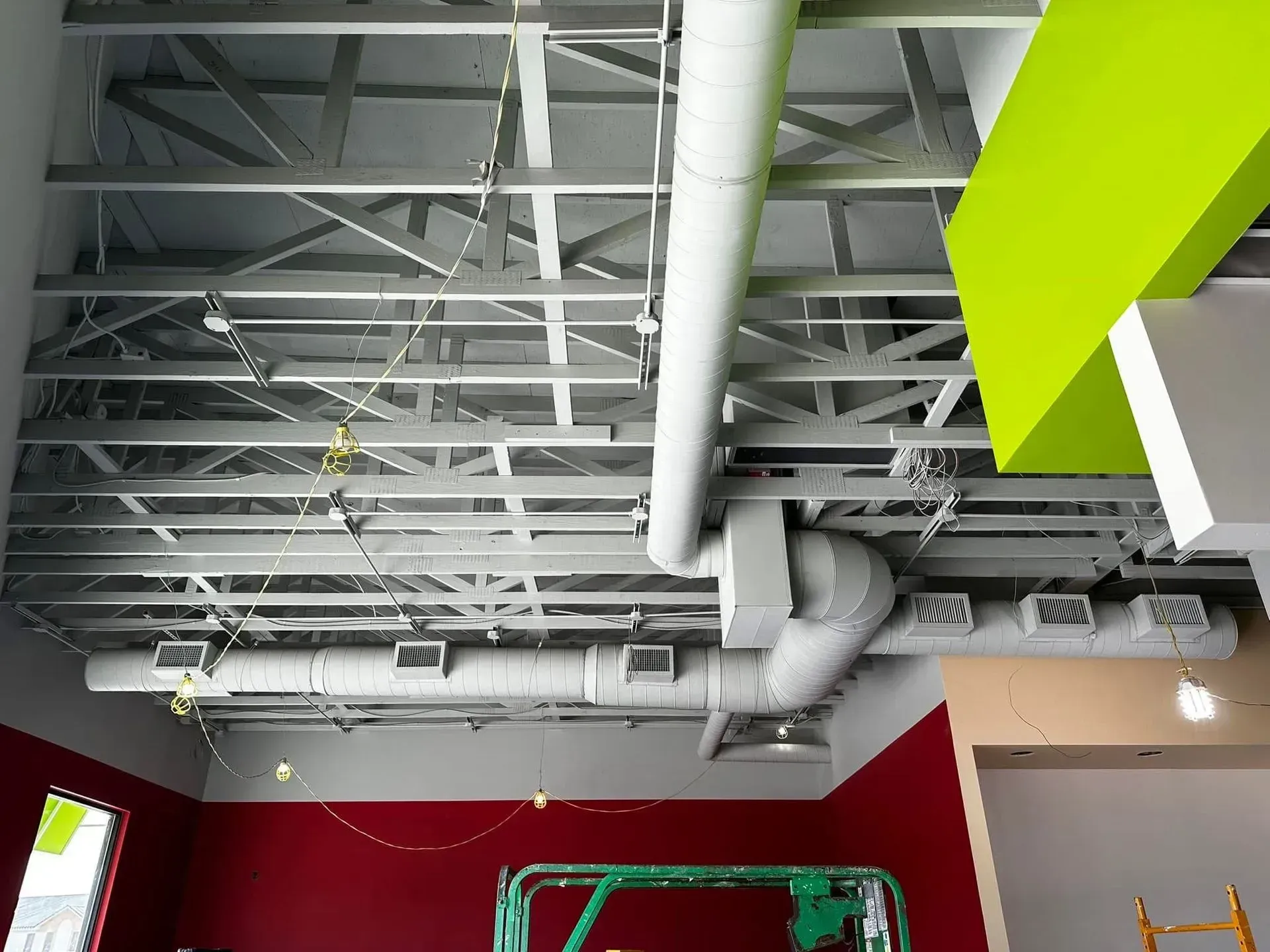 Industrial ceiling with exposed pipes, ducts, and beams above red and green walls