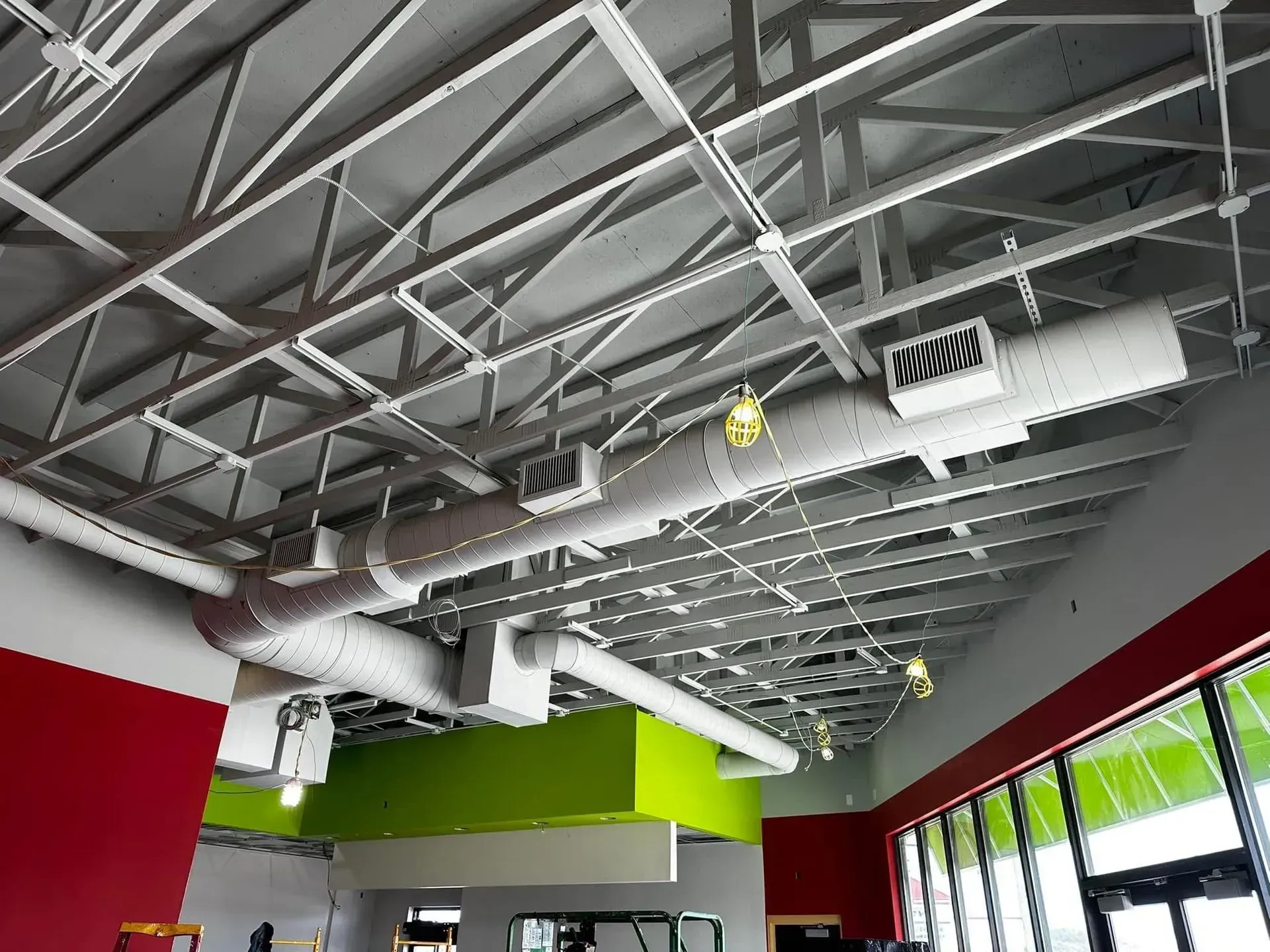 Industrial interior with exposed ceiling beams, red and green walls, and large windows.