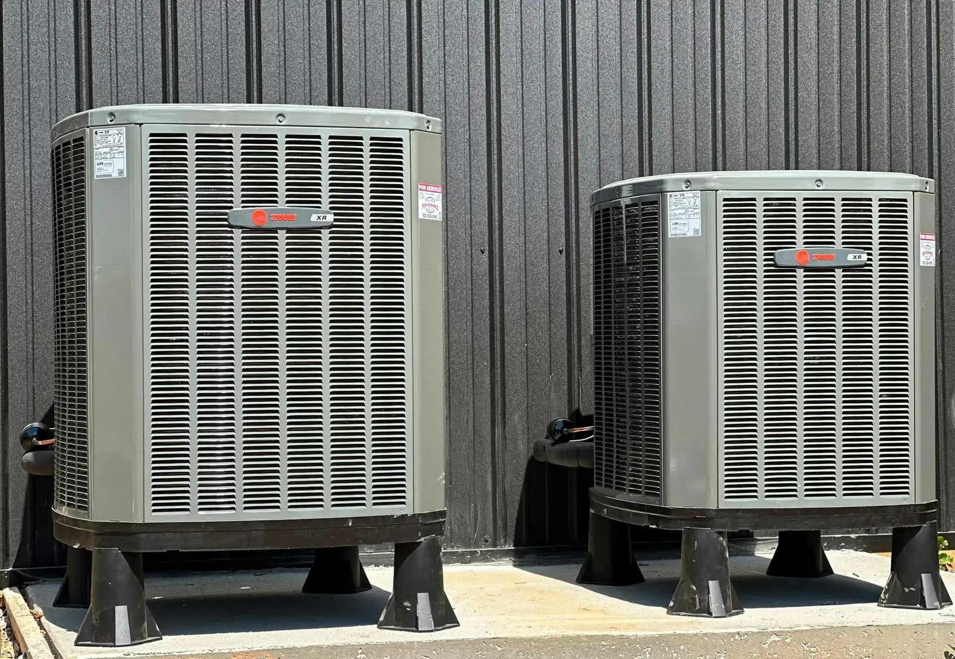 Two large outdoor HVAC units on stands beside a corrugated metal wall.
