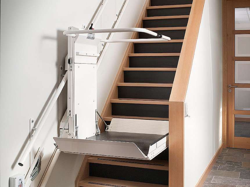 Stairlift on wooden stairs with a white wall, offering accessibility in a home.