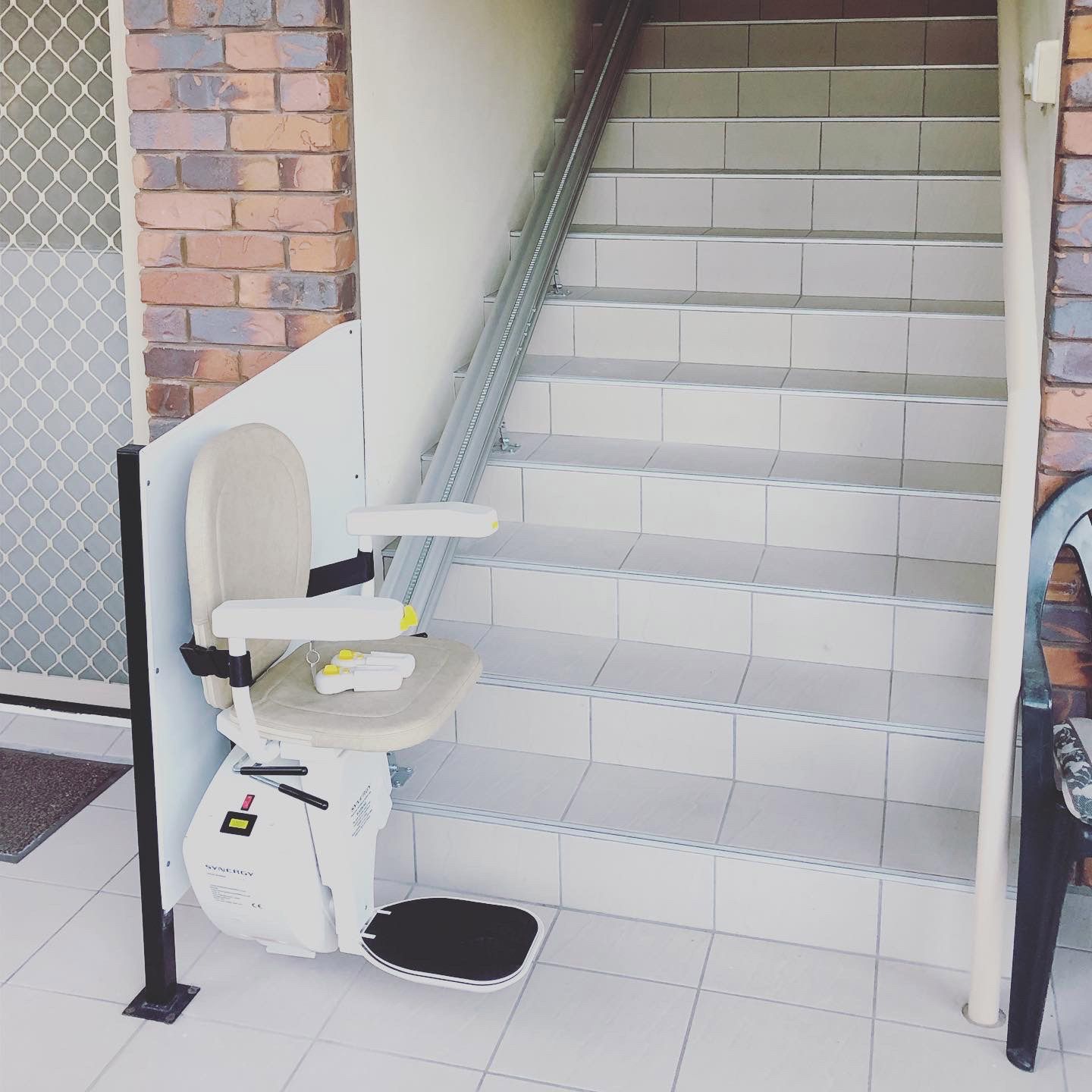 Stair lift installed on outdoor staircase next to a brick wall and a door.