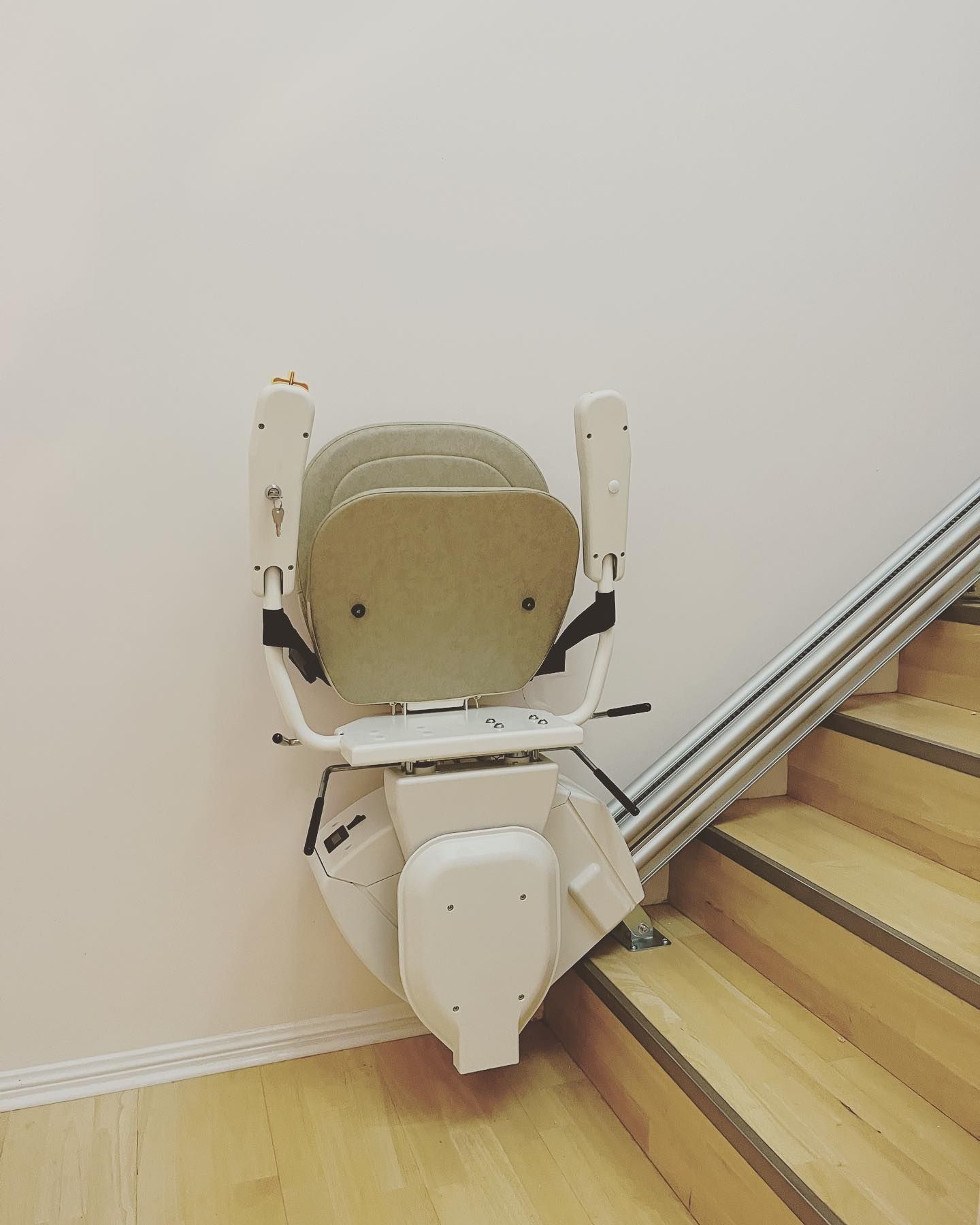 Stair lift attached to a staircase. The lift is beige and the stairs are wooden.