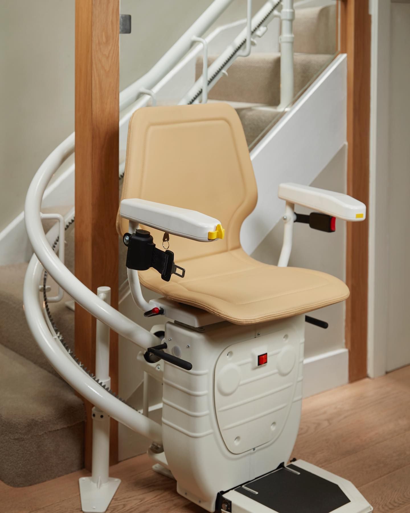 Beige stairlift on a staircase with a wooden post and white walls, for mobility assistance.