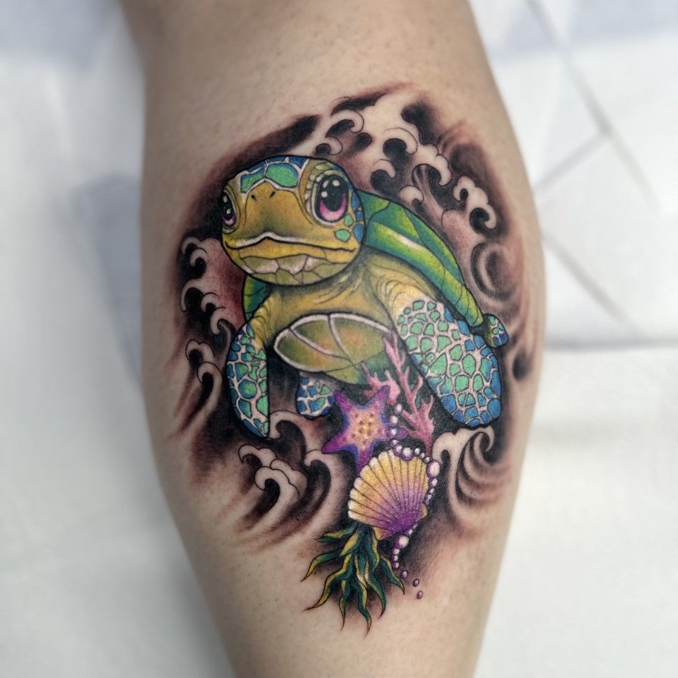 Tattoo of a cartoon sea turtle with blue and green shell, surrounded by waves, coral, and a seashell.