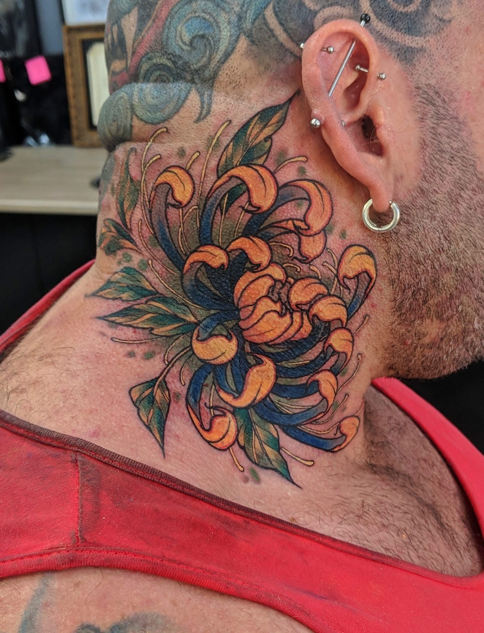Tattoo of Orange and Blue Flower With Green Leaves on a Persons Neck — Whitsunday Tattooing Airlie Beach in Airlie Beach, QLD