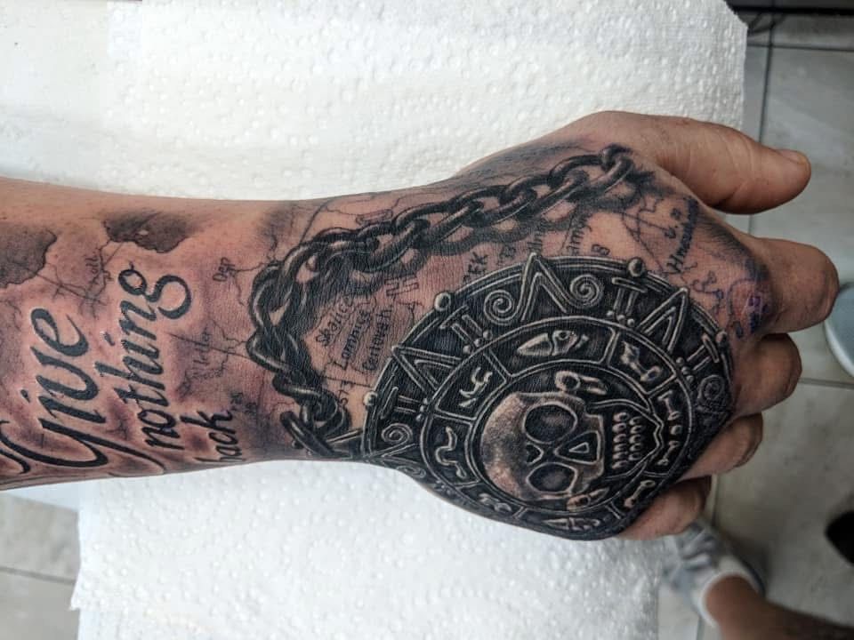 Tattoo on a hand. Includes a skull, chain, and text 