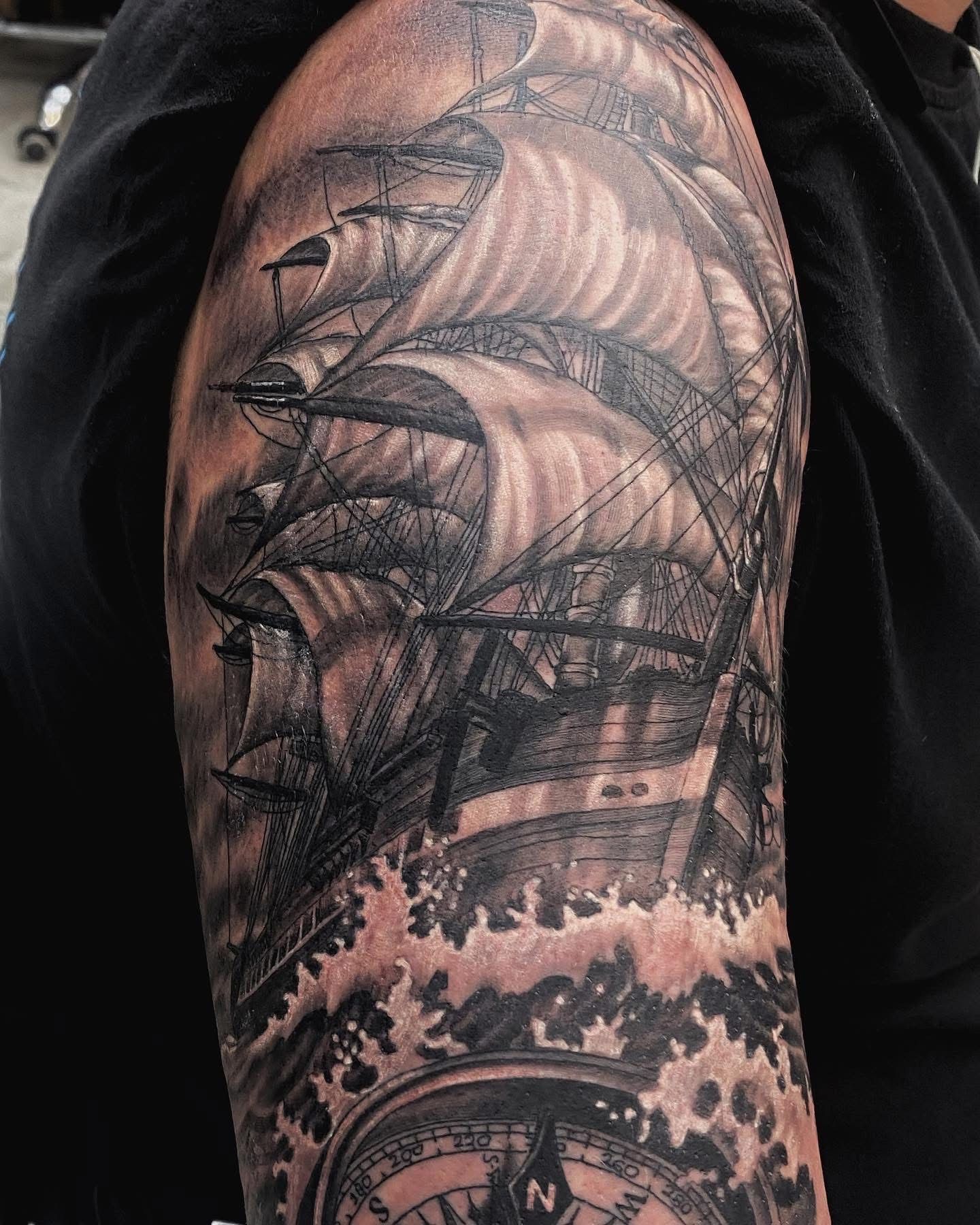 Black and gray ship tattoo on arm, in stormy seas with compass at the bottom. — Whitsunday Tattooing Airlie Beach in Whitsundays, QLD