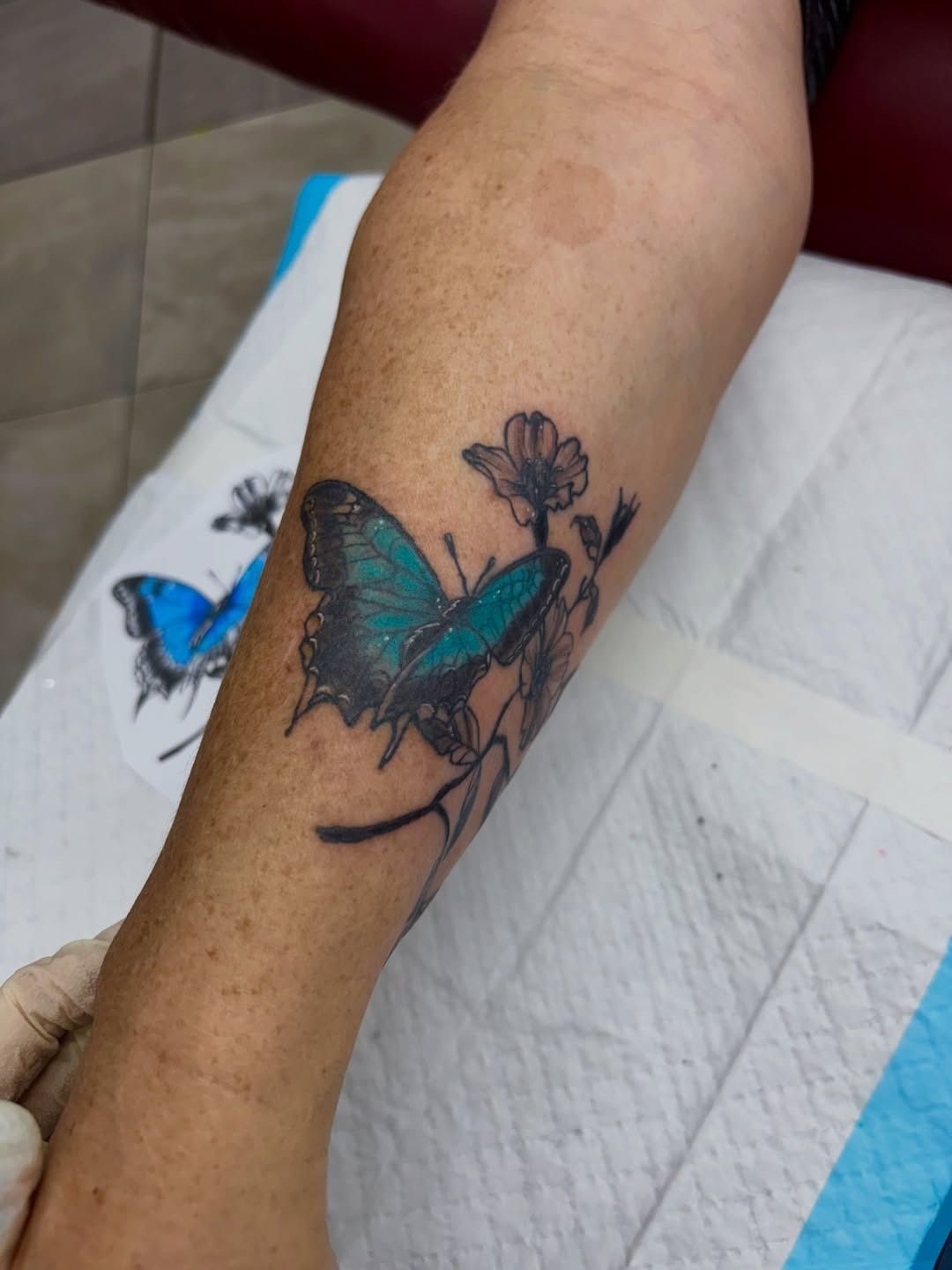 Tattoo of a blue butterfly on a forearm, with a small flower above it — Whitsunday Tattooing Airlie Beach in Whitsundays, QLD