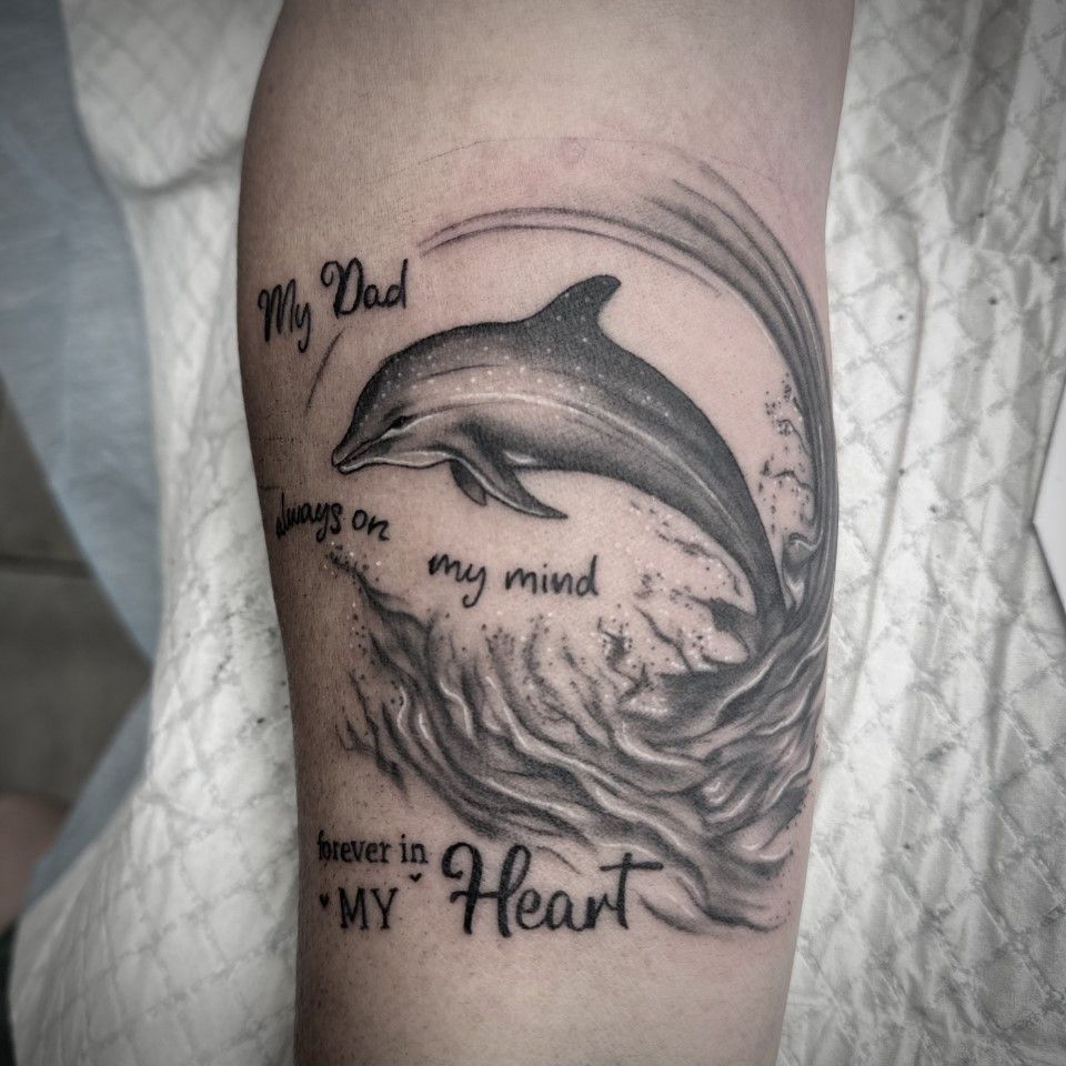 Tattoo of a dolphin leaping from water, text says 