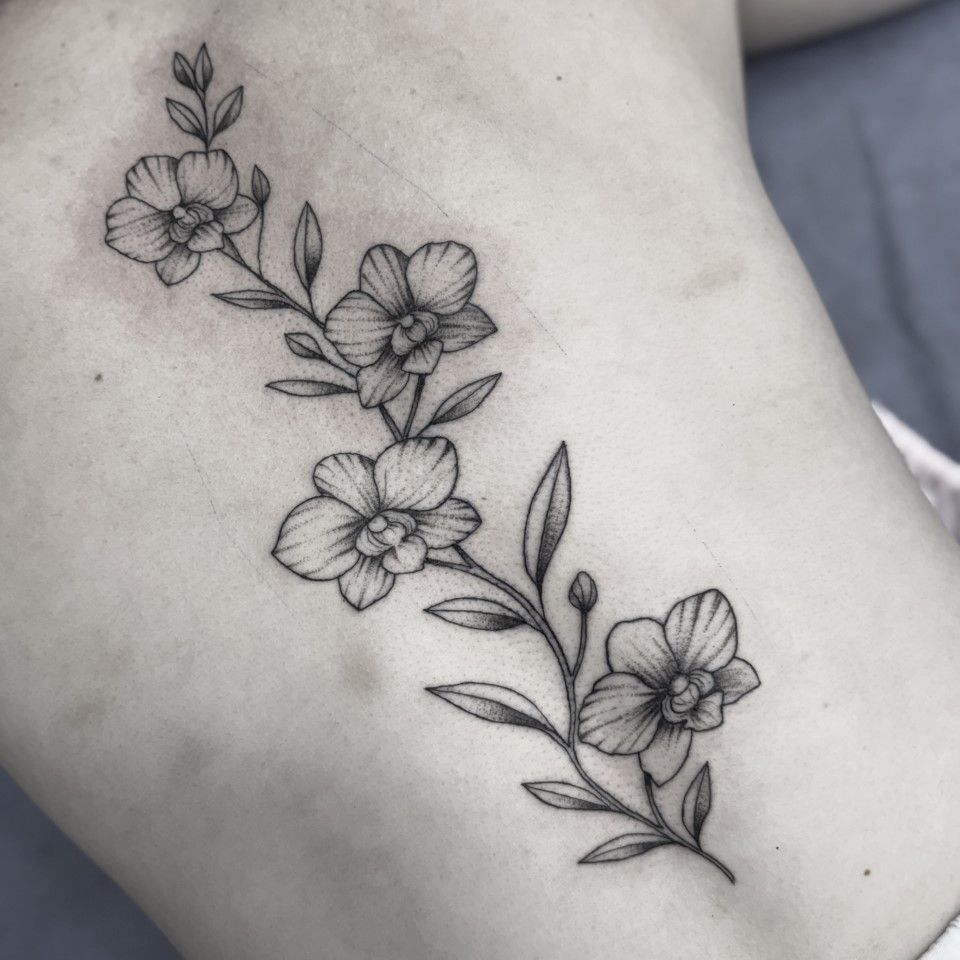 Black ink floral tattoo on a back, featuring a flowering branch with detailed petals and leaves. — Whitsunday Tattooing Airlie Beach in Whitsundays, QLD