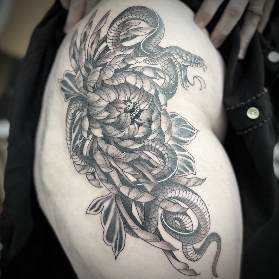 Black and gray tattoo of a snake coiled around a large flower on a person's thigh.