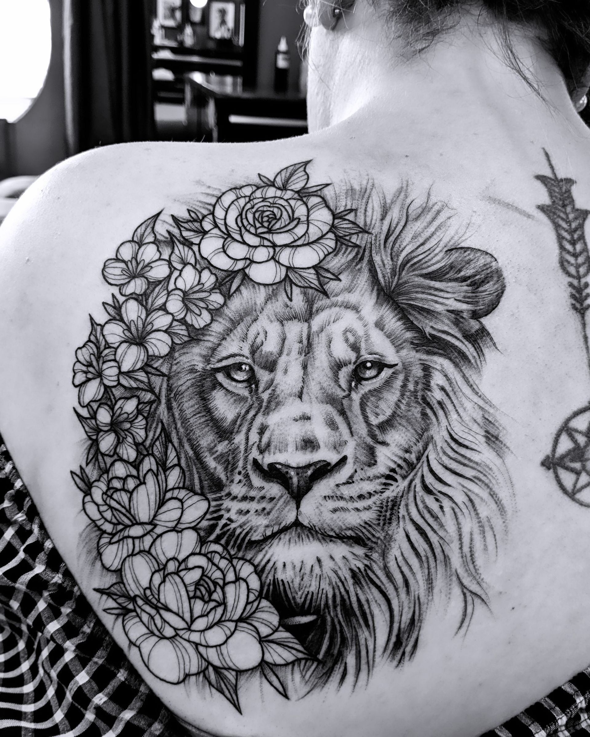 Lion tattoo with floral crown on a person's back; black and white.