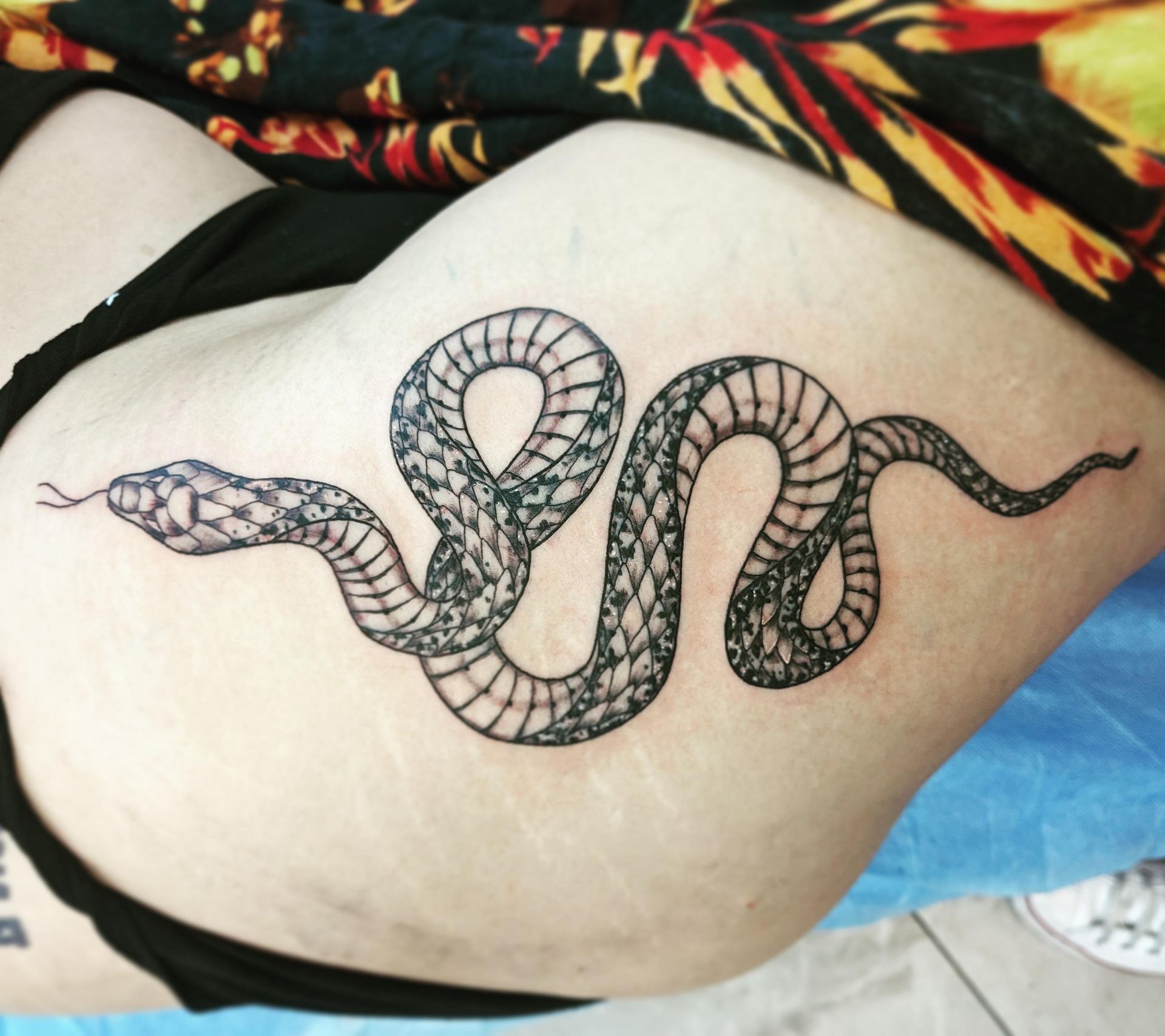 Black snake tattoo coiled on a person's side, with scales detailed in fine lines.