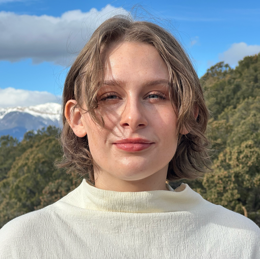 Mel Garvin with short brown hair, smiling in front of snow-capped mountains and a blue sky.