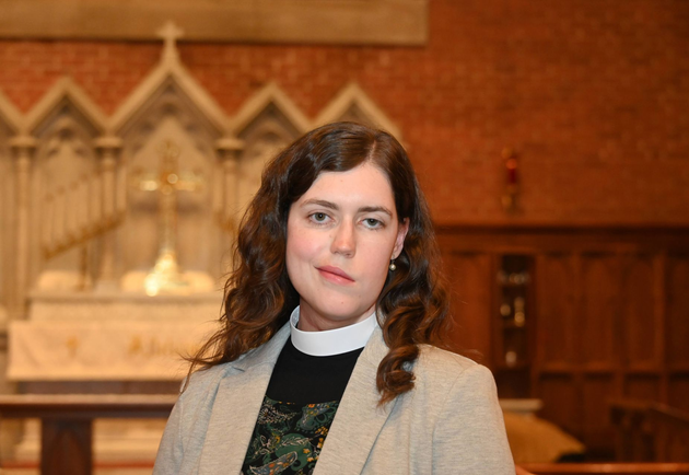 Mother Cat in a gray blazer and clerical collar standing in a church interior