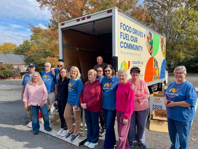 Volunteers posing beside a food drive truck with “Food Drive for our Community” sign.