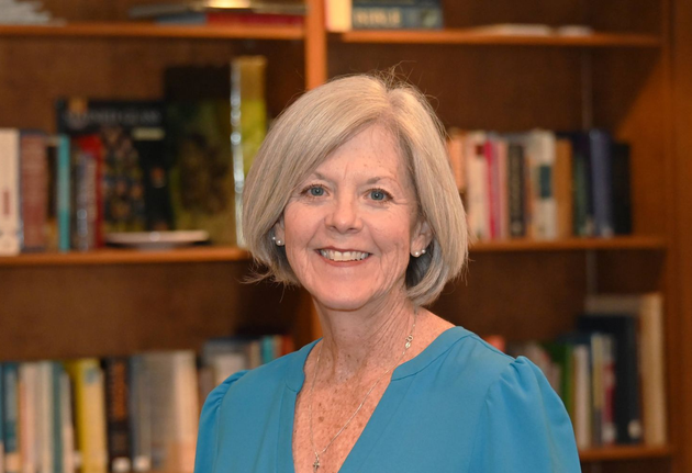 Lauren Cavins in a blue blouse standing in front of bookshelves