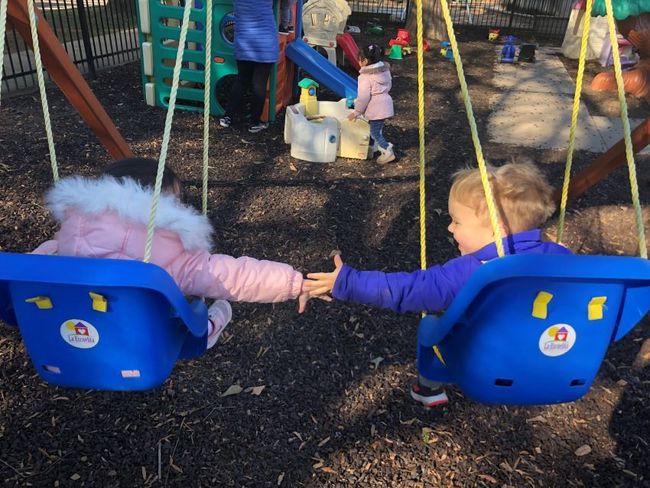 Two children reaching for hands while sitting on blue swings in a playground