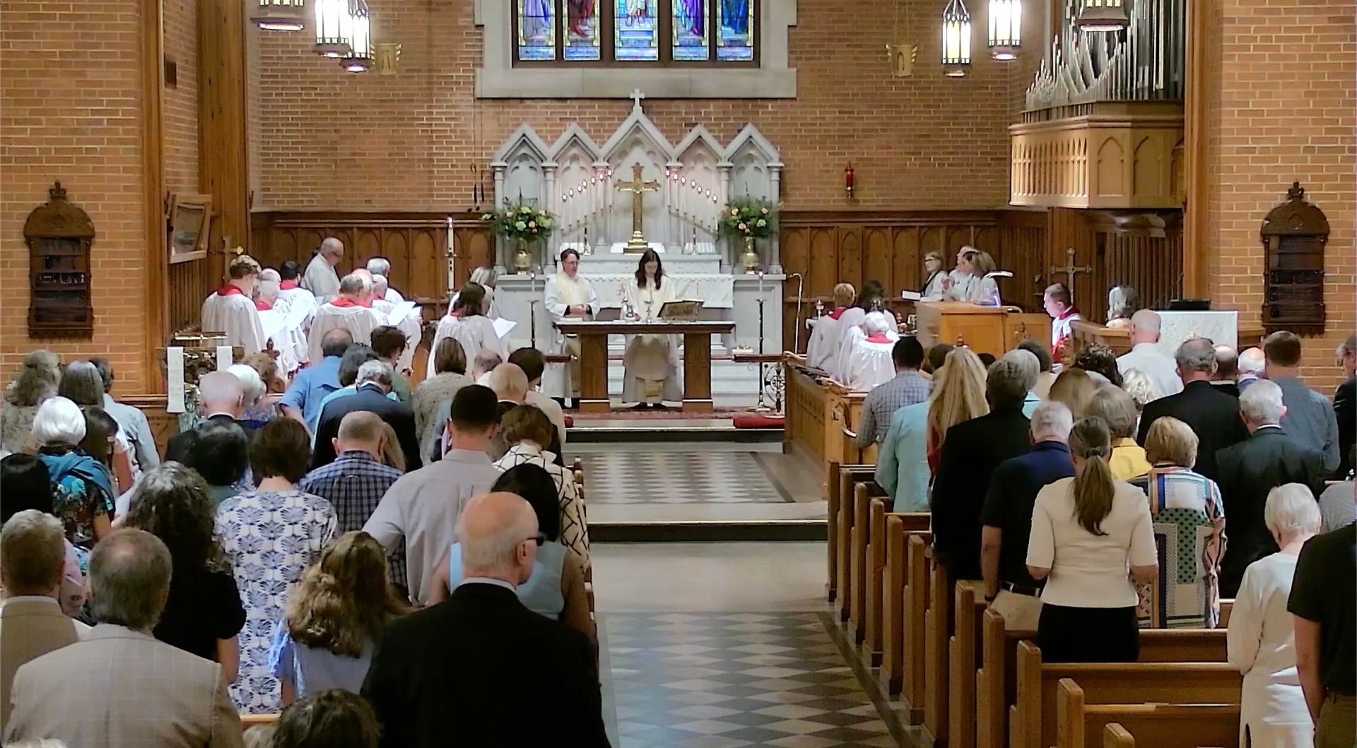 Congregation standing in a church during a service, facing the altar and priest.