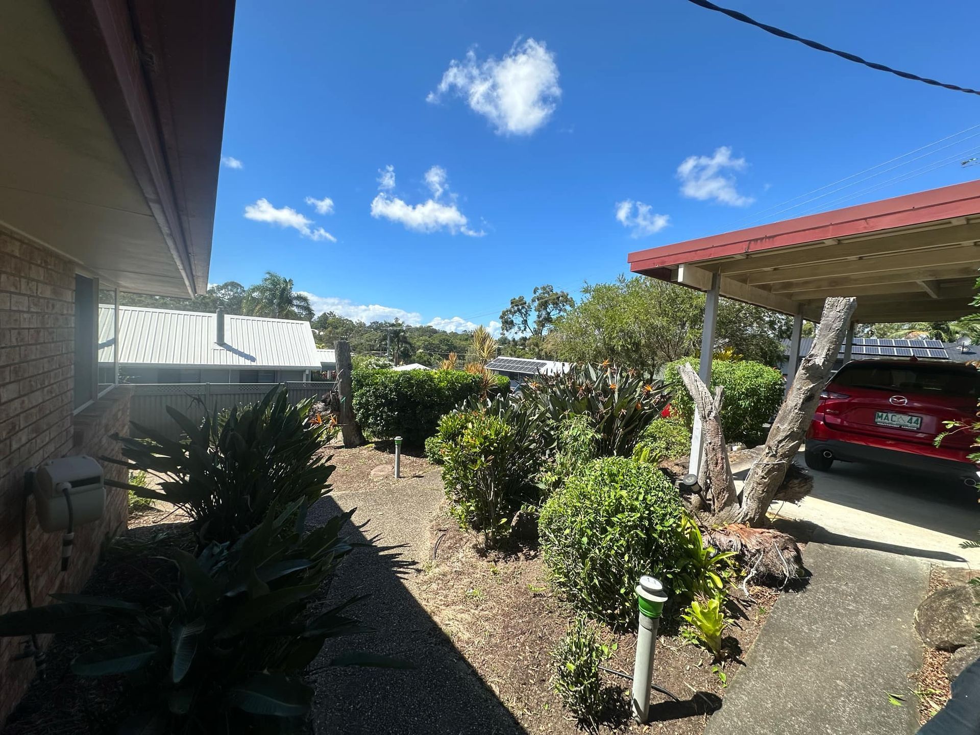 A red car is parked under a carport in front of a house | MowAbility Garden Services Gold Coast
