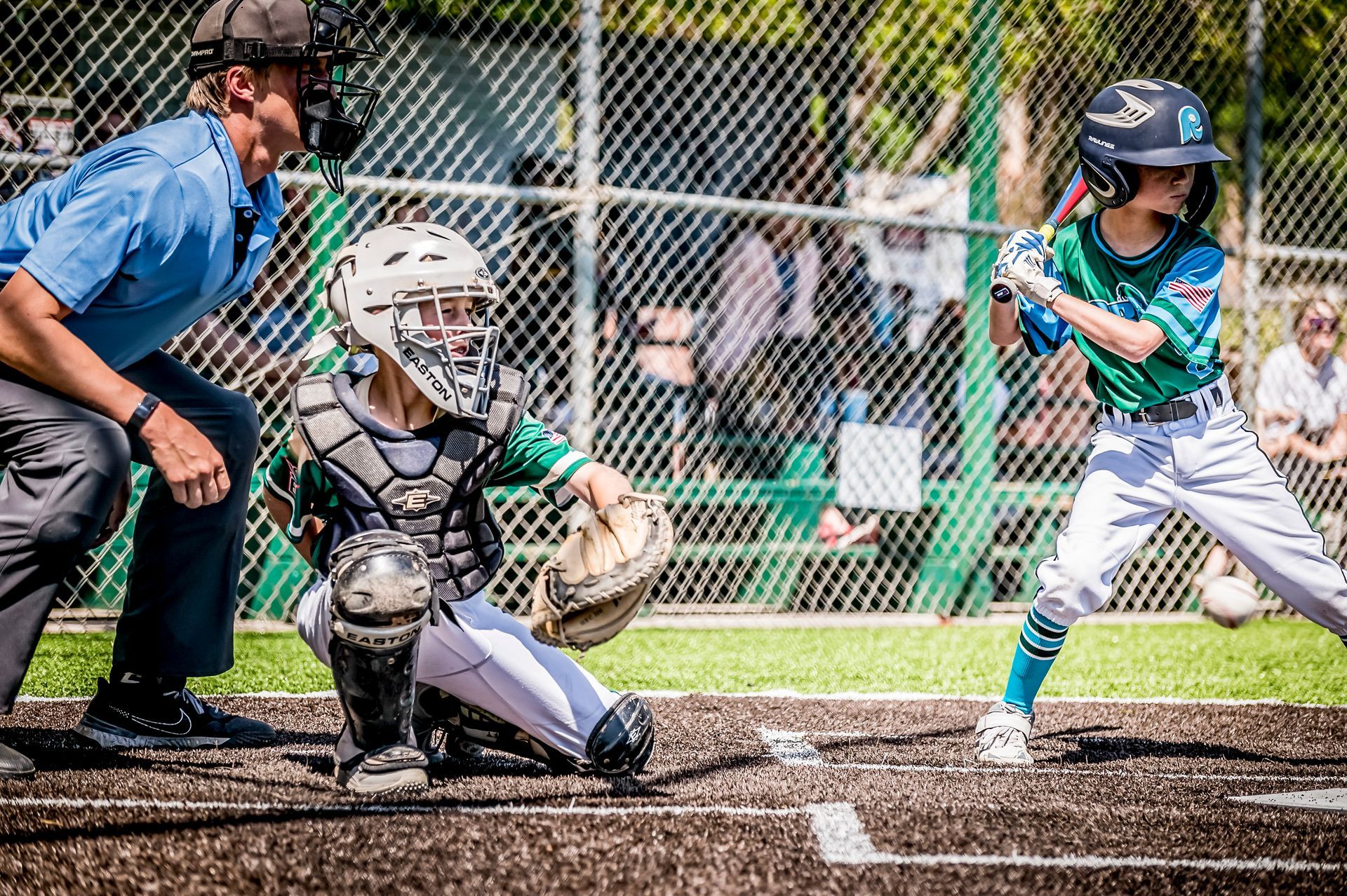 Youth baseball game at home plate, catcher crouched and batter in blue ready to swing.