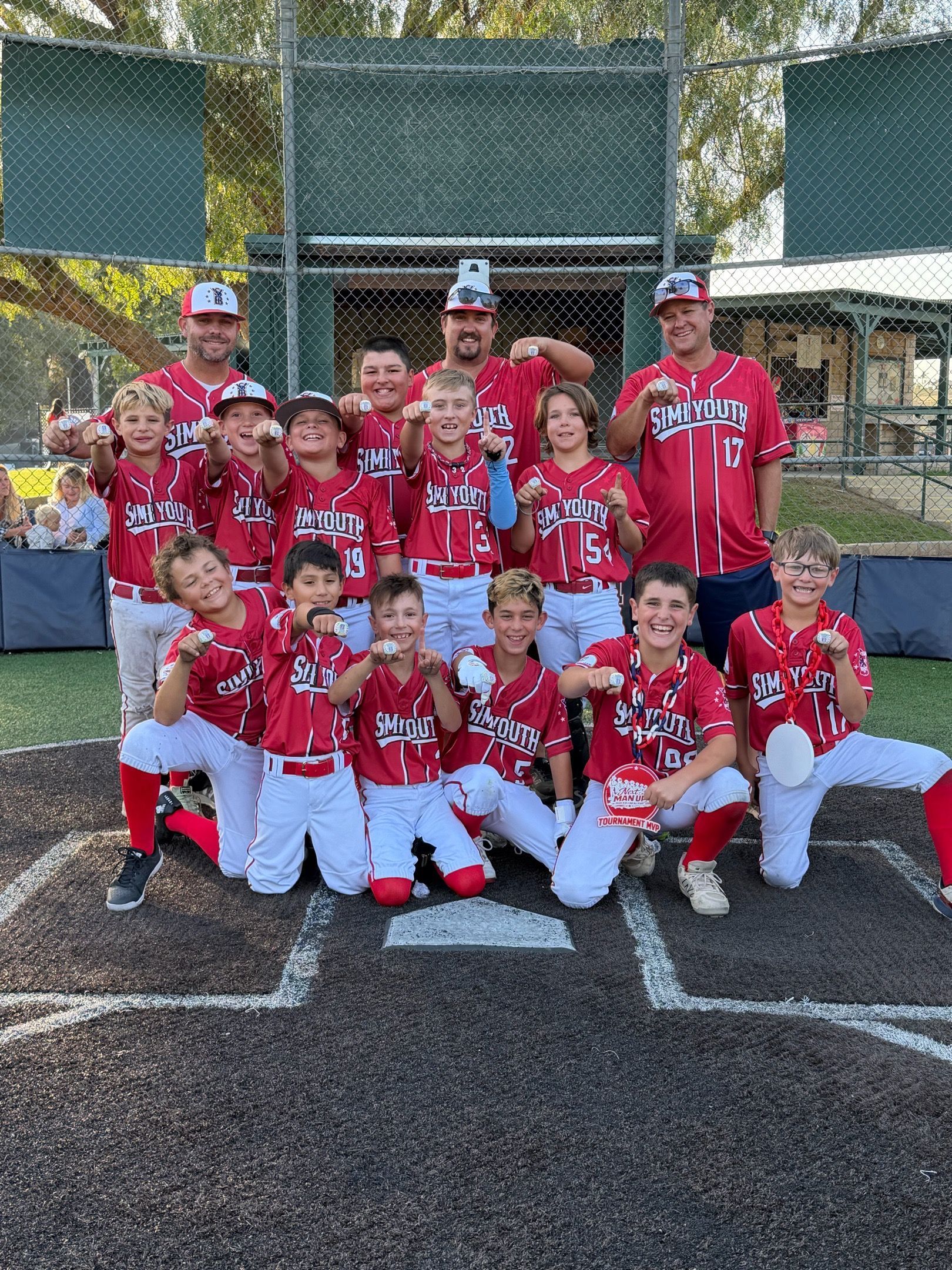 Youth softball team in red uniforms posing on a field with coaches behind them