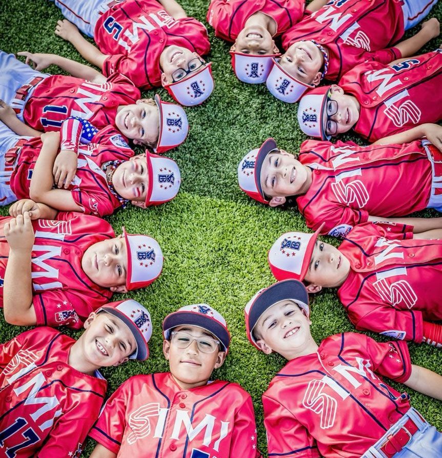 A group of baseball players in red uniforms and caps lying in a circle on grass, smiling up at the camera