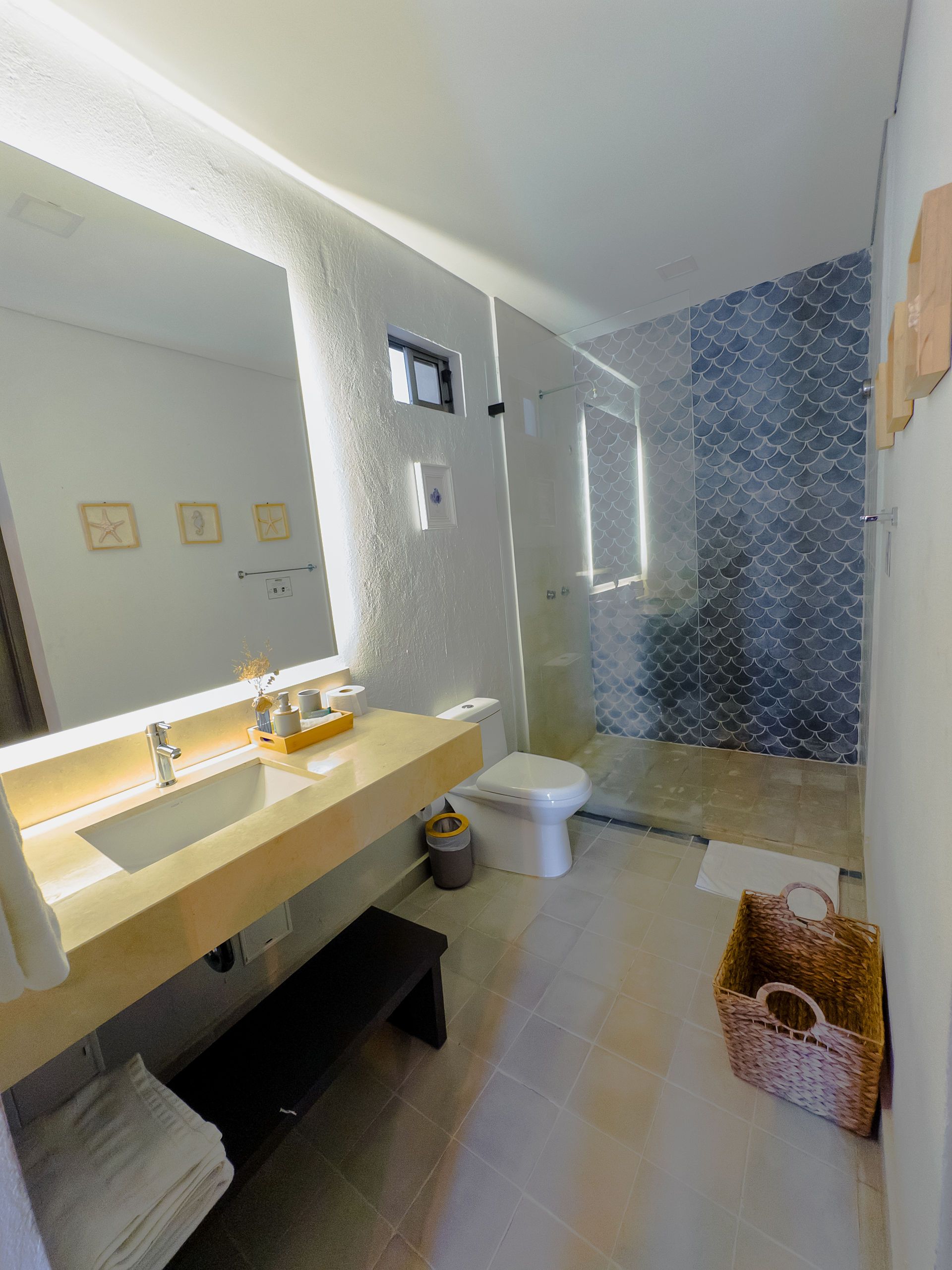 Baño moderno con tocador beige, ducha de vidrio y pared decorativa estampada.