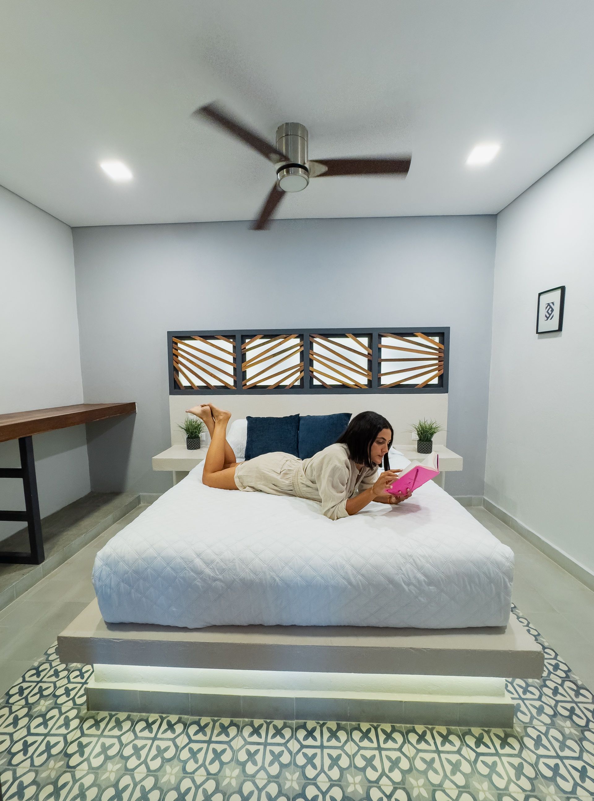 Mujer leyendo en una cama en un dormitorio moderno con cabecero decorativo.