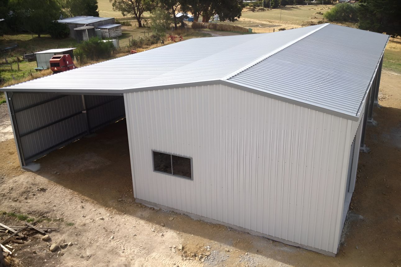 A Large White Building With a Gray Roof is Sitting on Top of a Dirt Field — Mareeba Sheds & Gas In Cairns, QLD