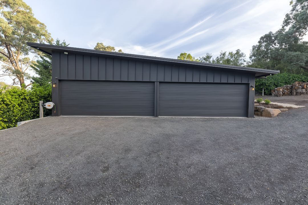 A Black Garage Door is Sitting on Top of a Gravel Driveway — Mareeba Sheds & Gas In Mareeba, QLD