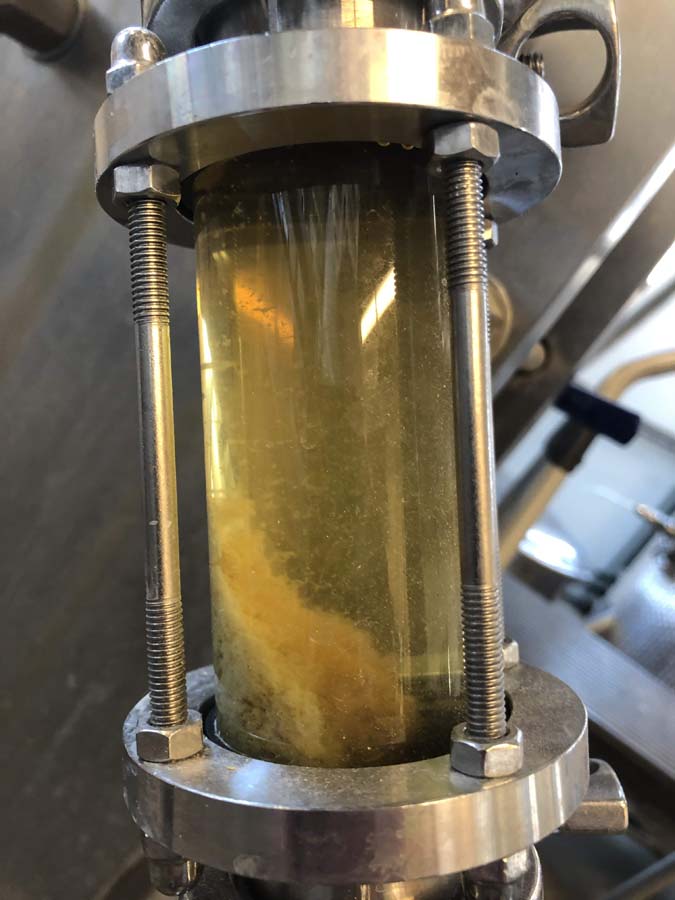A close up of a stainless steel pipe with a bottle of liquid in it.