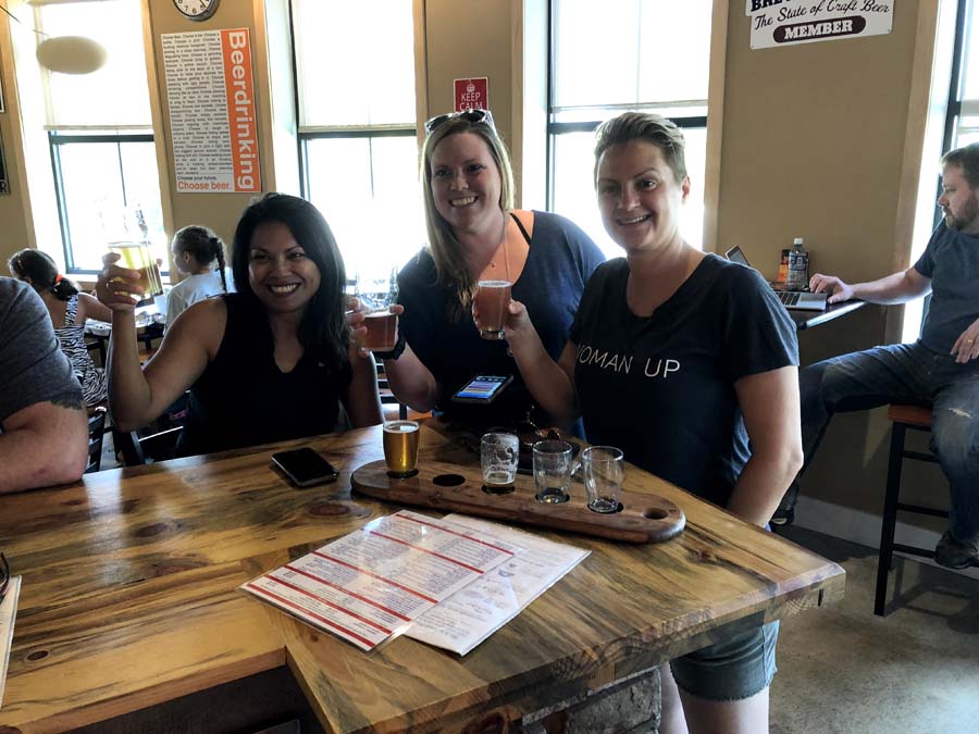 Three women are sitting at a table holding glasses of beer.
