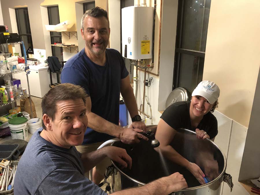 A group of people are standing around a large pot in a kitchen.
