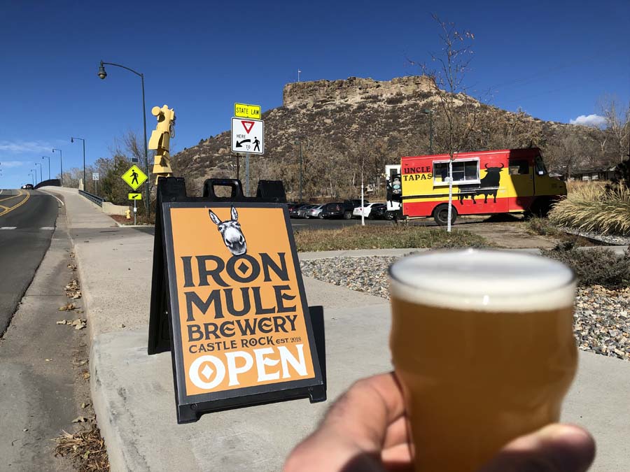 A person is holding a glass of beer in front of a sign that says iron mule brewery open