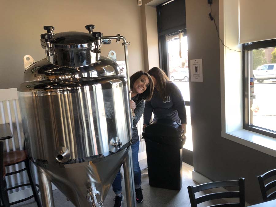 Two women are standing in front of a large stainless steel tank.