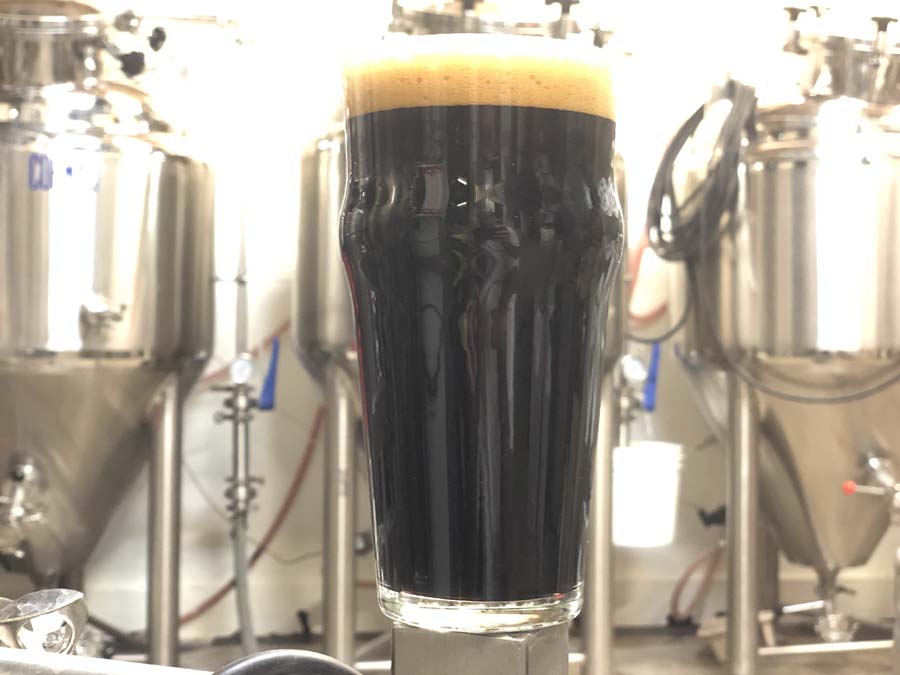 A glass of dark beer is sitting in front of a brewery
