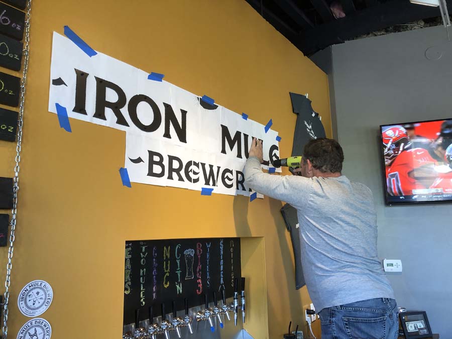 A man is hanging a sign on a wall that says iron mill brewery