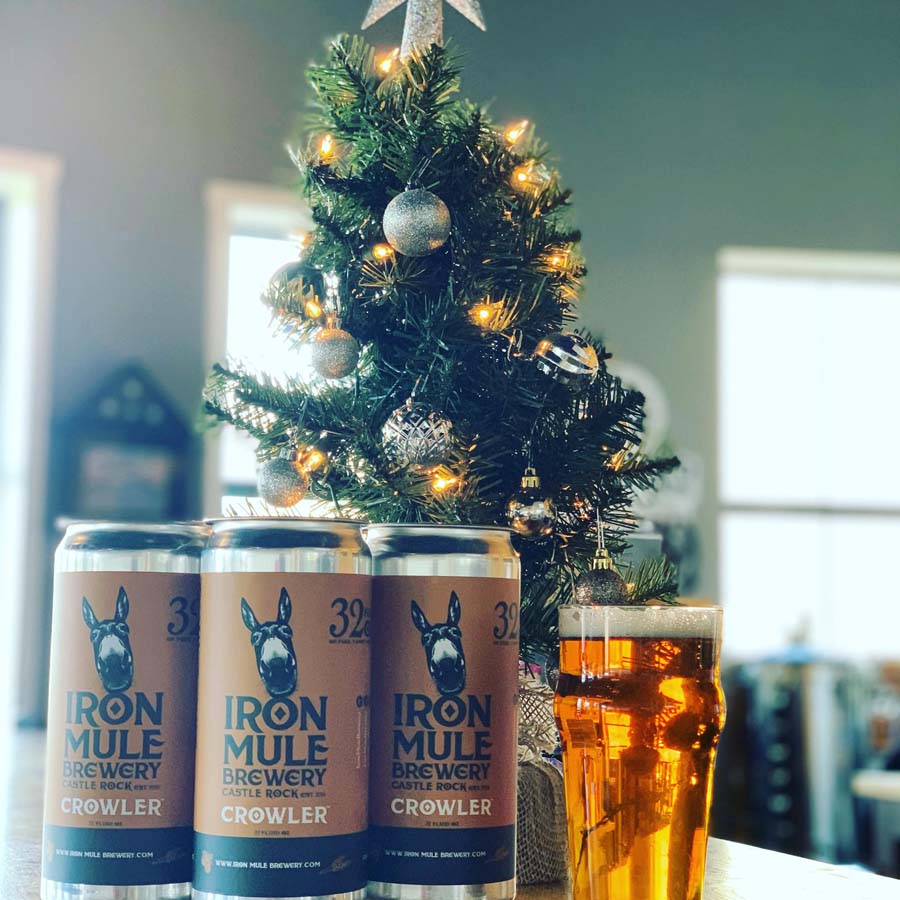 Three cans of iron mule brewery crowler next to a christmas tree