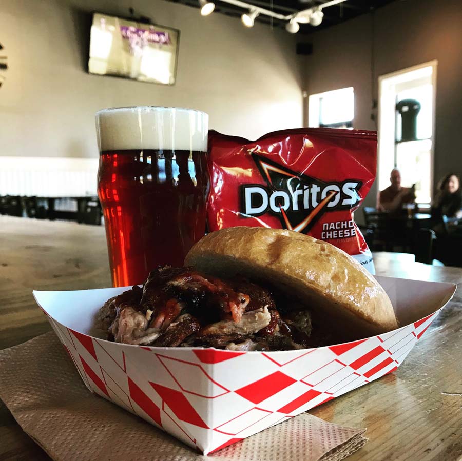 A sandwich with a bag of doritos next to a glass of beer