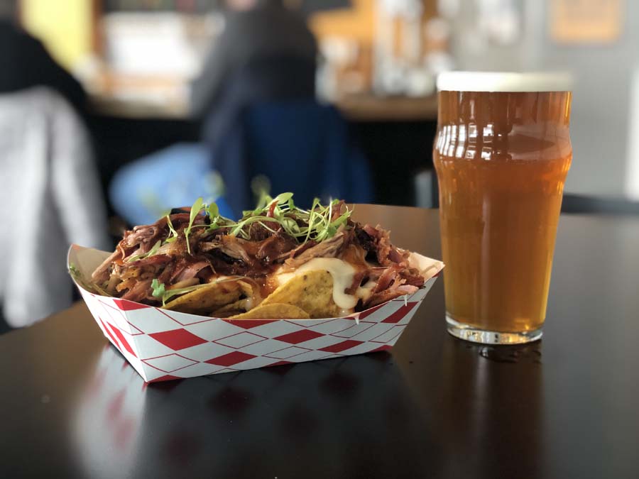 A tray of food and a glass of beer on a table.