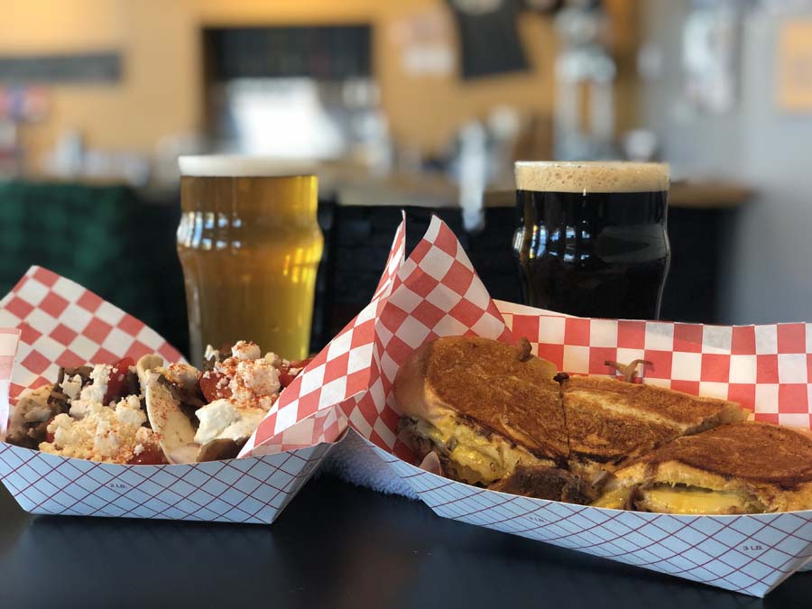 Two trays of food and two glasses of beer on a table.
